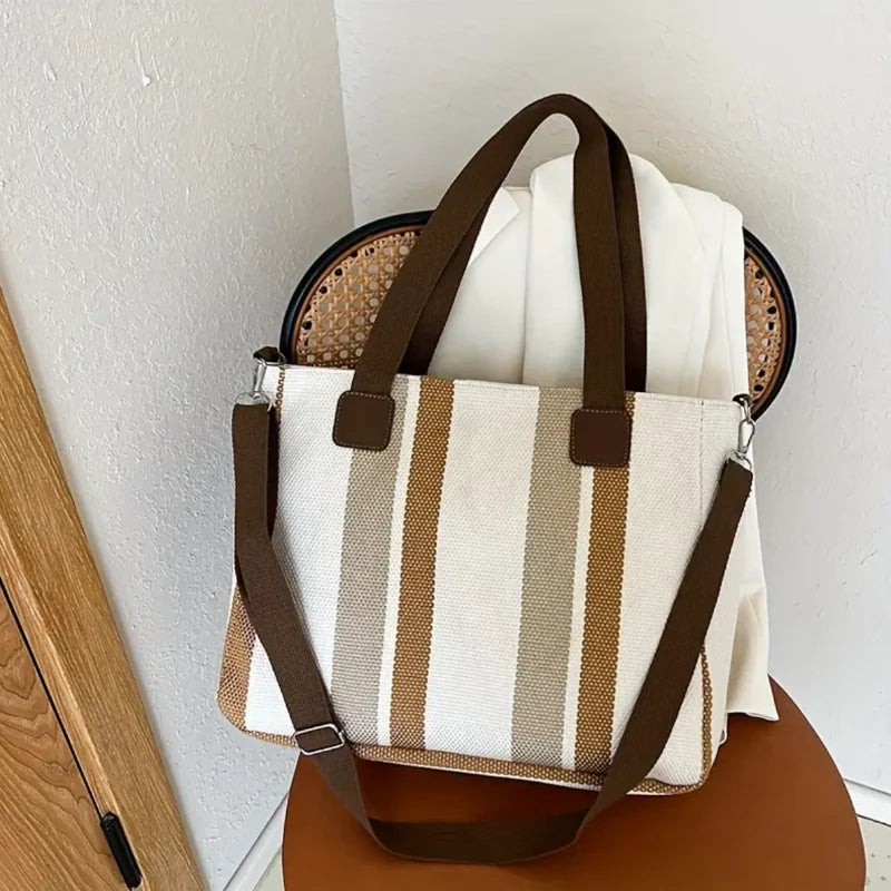 Bolsa feminina grande com alça longa e alças curtas, em tecido texturizado com listras em tons neutros. Design funcional e elegante para uso diário.