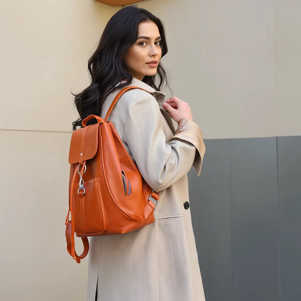 Mulher usando mochila feminina laranja com acabamento em couro sintético, combinando com casaco bege. Design elegante e funcional para uso diário, trabalho ou passeios urbanos.