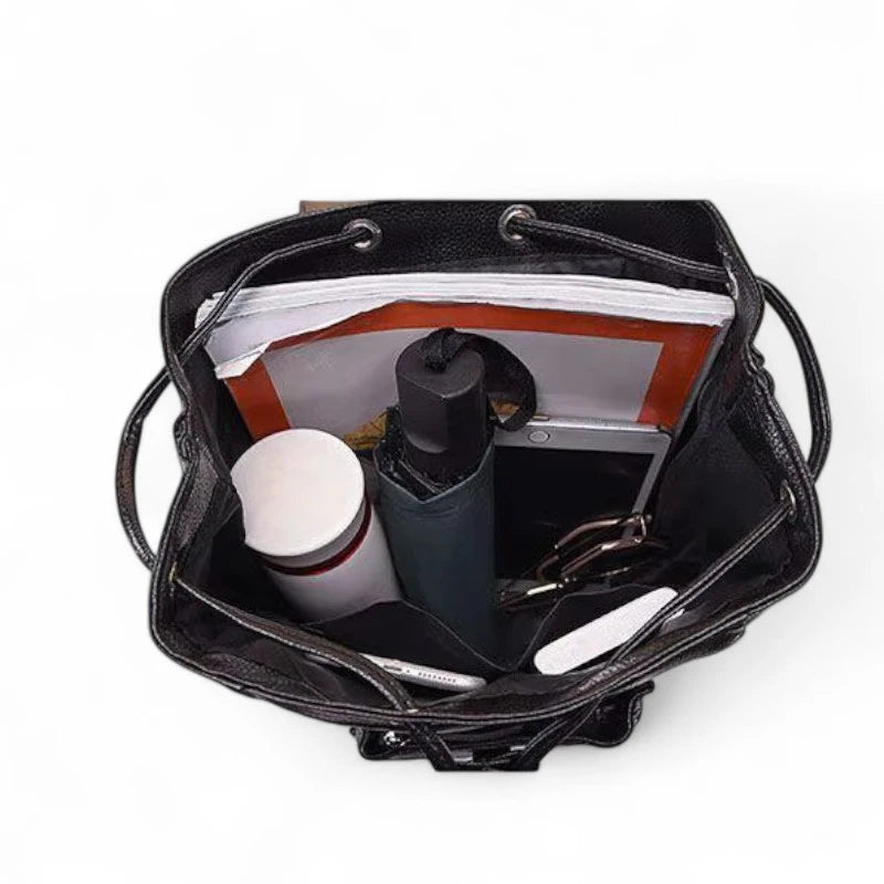 Interior da mochila feminina preta com compartimentos organizados, contendo notebook, caneca, guarda-chuva e documentos. Espaço amplo e prático para uso no trabalho, estudo ou viagem.
