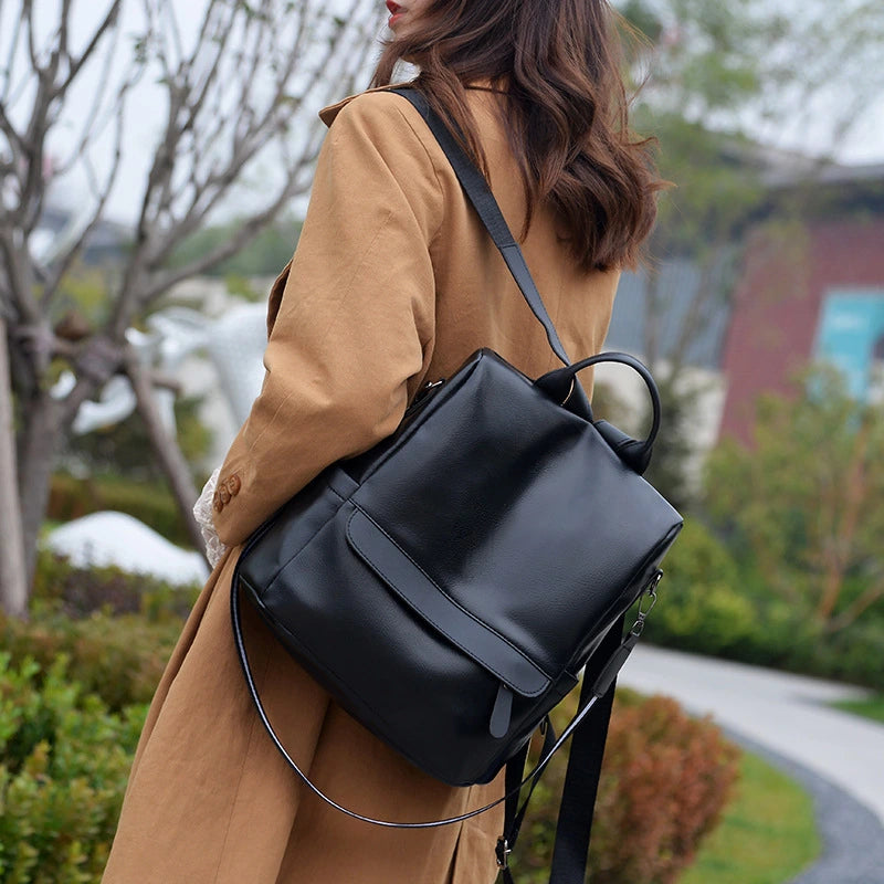 Mulher usando mochila feminina preta com alça transversal, combinando com look elegante de casaco marrom. Design moderno e versátil para uso diário, trabalho ou passeios urbanos.