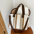 Bolsa feminina grande com alça longa e alças curtas, em tecido texturizado com listras em tons neutros. Design funcional e elegante para uso diário.