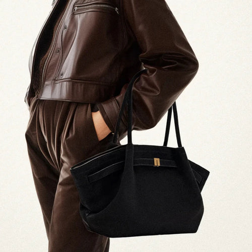 Mulher usando a bolsa feminina preta, combinada com jaqueta de couro marrom e calça de veludo