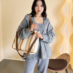 Mulher usando bolsa feminina transversal listrada em tons neutros, combinando com look casual de cardigan e calça. Ideal para uso urbano e rotina diária.