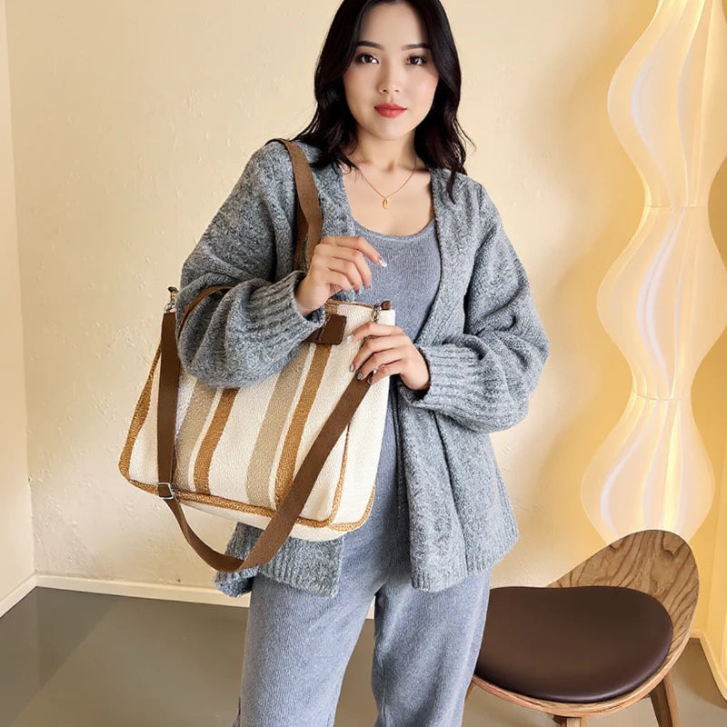 Mulher usando bolsa feminina transversal listrada em tons neutros, combinando com look casual de cardigan e calça. Ideal para uso urbano e rotina diária.