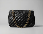 Vista traseira da bolsa Paris preta acolchoada, detalhando o design clássico com bolso externo discreto e alça em corrente dourada