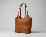 Bolsa feminina estilo tote em couro PU trançado na cor caramelo com alças de ombro finas e design de luxo minimalista em ângulo lateral.