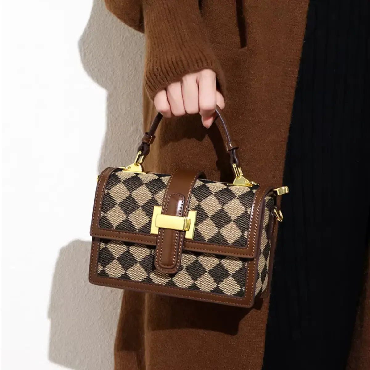 Modelo segurando a bolsa transversal feminina Isabela marrom xadrez com alça de corrente dourada