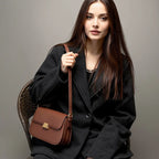 Mulher usando bolsa transversal feminina marrom com alça ajustável e fecho dourado.