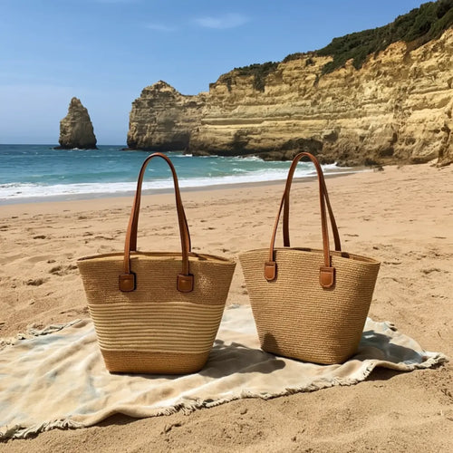 Duas bolsas femininas grandes de palha com alças marrons sobre toalha na praia.